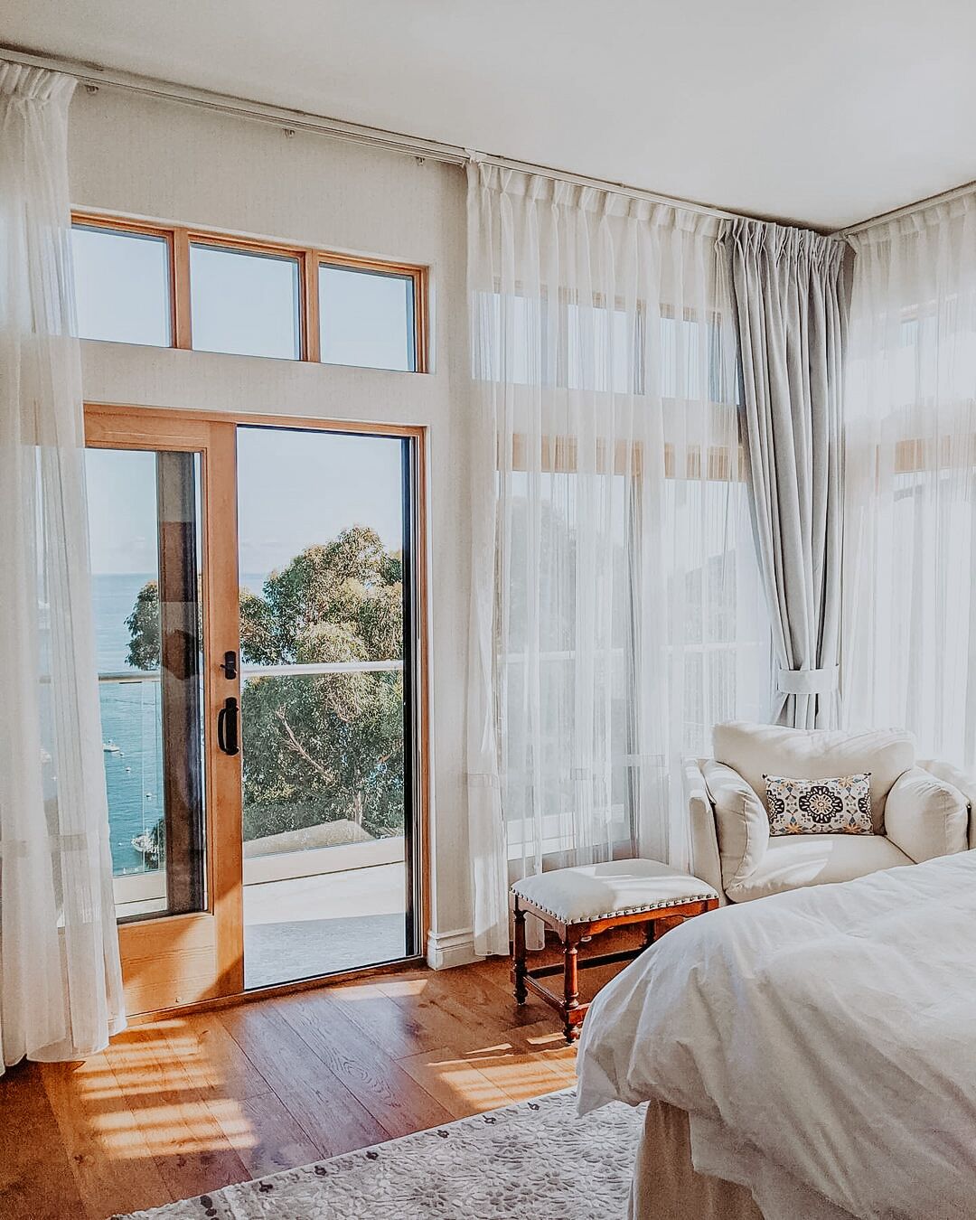 Une chambre avec une grande porte-fenêtre coulissante donnant sur un balcon, un lit, une chaise et des rideaux légers.