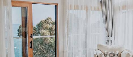 Une chambre avec une grande porte-fenêtre coulissante donnant sur un balcon, un lit, une chaise et des rideaux légers.