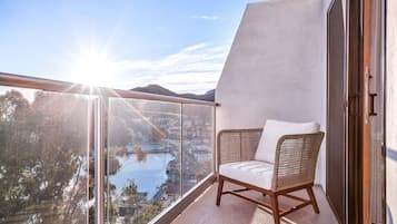 Ein Balkon mit einem Korbstuhl, einer Glastür und Blick auf eine Stadtlandschaft und Wasser.