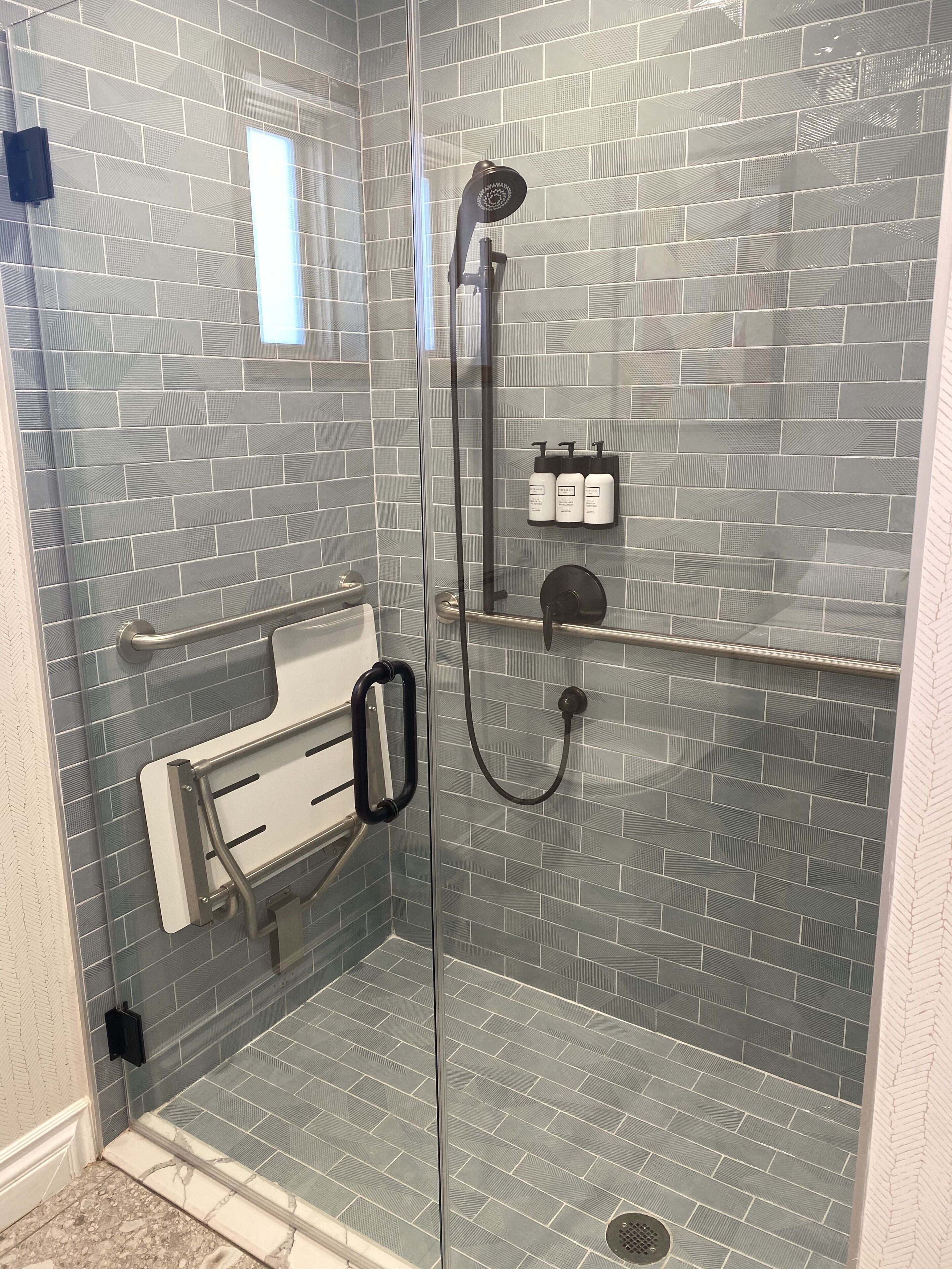 A walk-in shower with a glass door, a handheld showerhead, a handheld showerhead, and a soap dispenser.