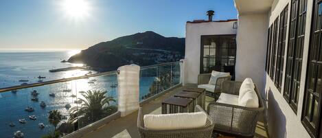 A balcony with wicker furniture, a view of the sea, and boats.