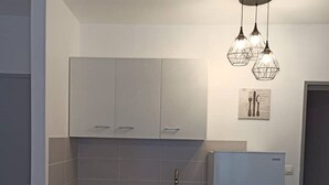 Una cocina compacta con armarios blancos, un lavamanos de acero inoxidable, un horno empotrado y un refrigerador.