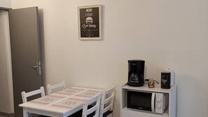 Una pequeña cocina americana con una mesa y sillas blancas, un microondas y una cafetera.