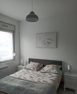A bedroom with a bed, two bedside tables, a hanging light, and a wall-mounted artwork.
