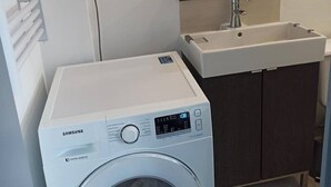 Un lavadero pequeño con una lavadora Samsung, un lavabo y un armario de madera oscura.