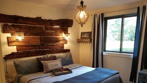Een slaapkamer met een houten hoofdbord, een bed met een gewatteerde sprei, een nachtkastje en een raam met gordijnen.