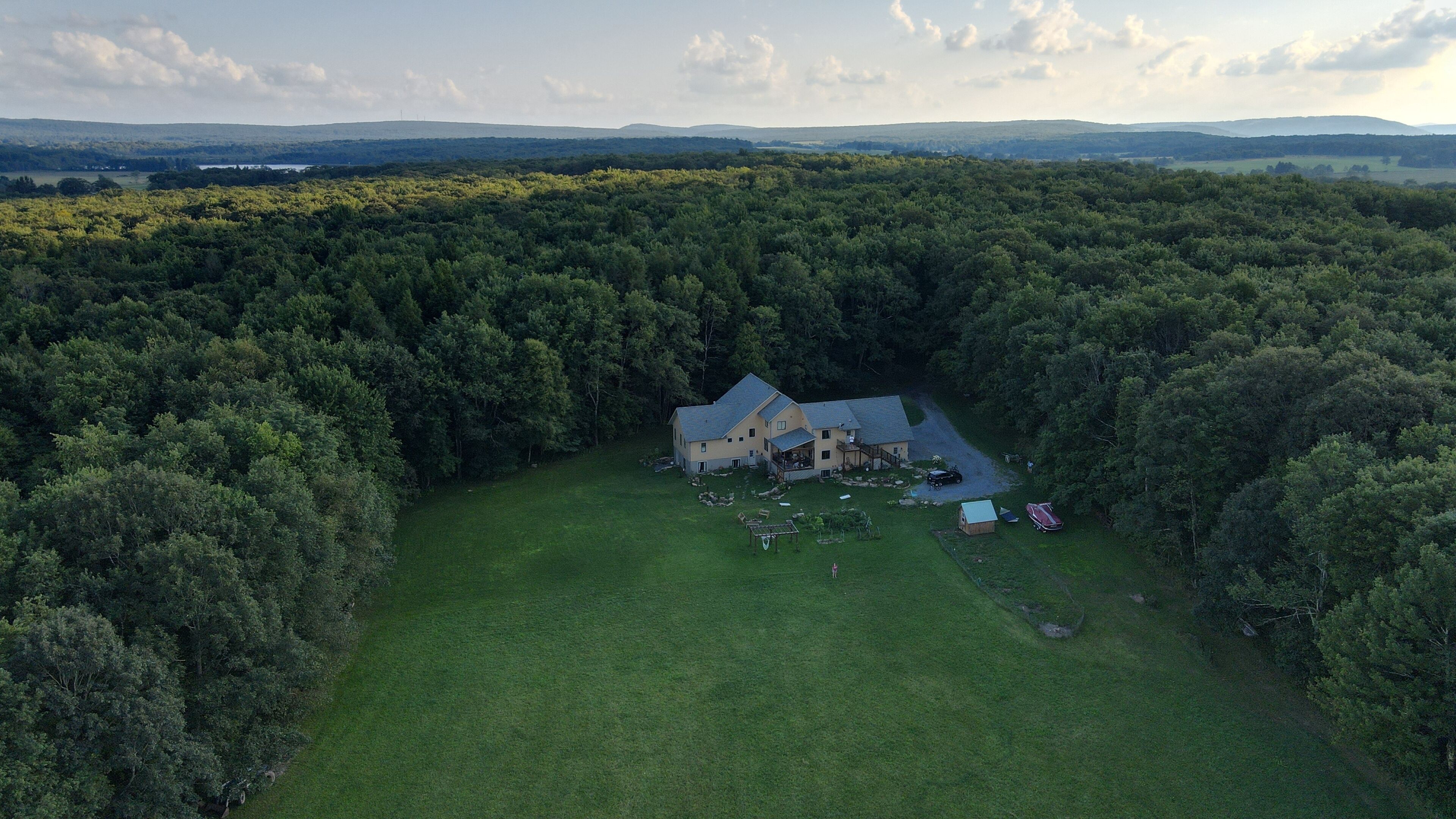 Une vue aérienne d’une grande maison entourée d’une forêt dense, avec une pelouse bien entretenue et une allée menant à l’entrée.