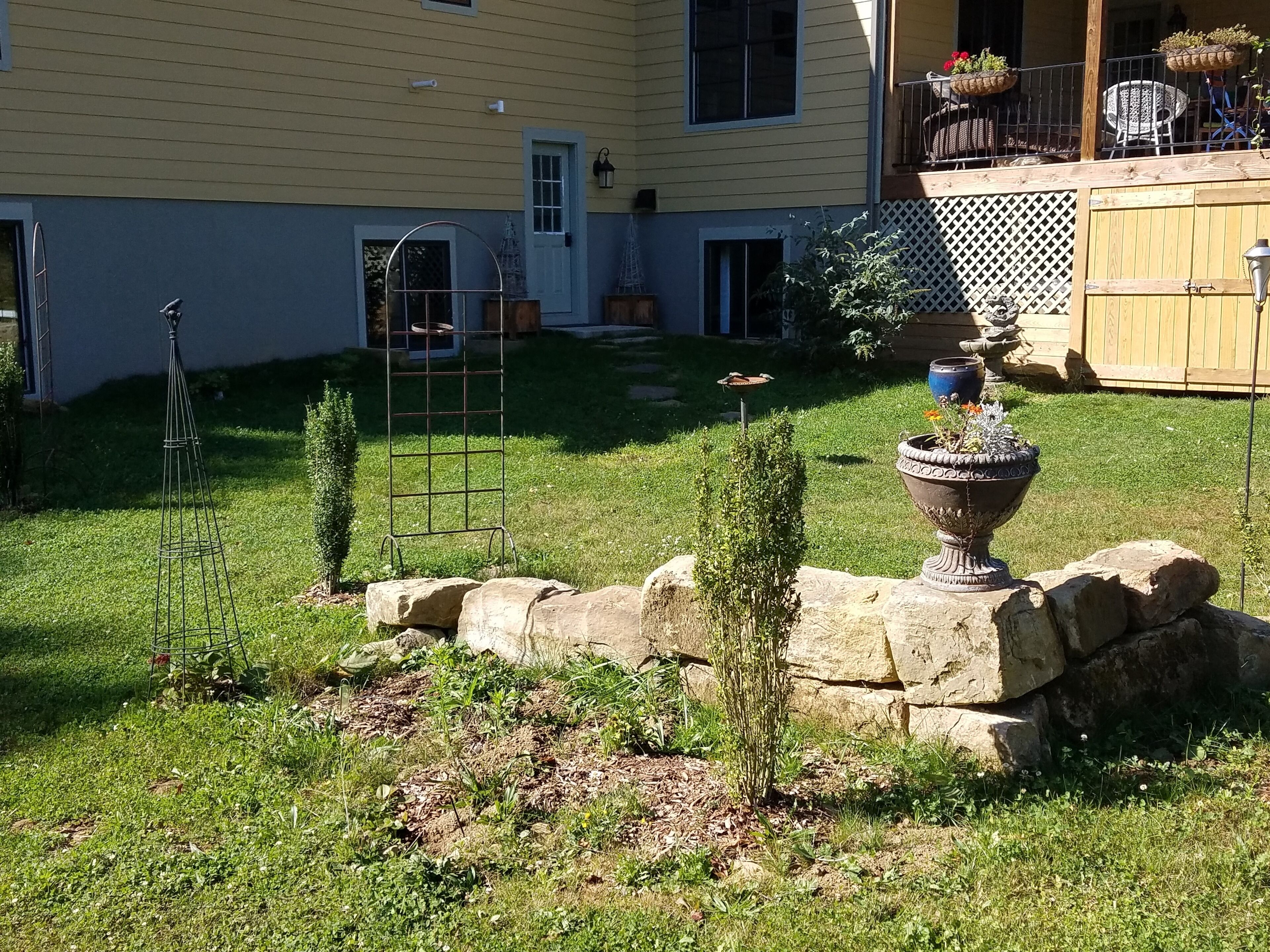 Un patio trasero bien cuidado con un muro de piedra, un comedero para pájaros y una urna decorativa.
