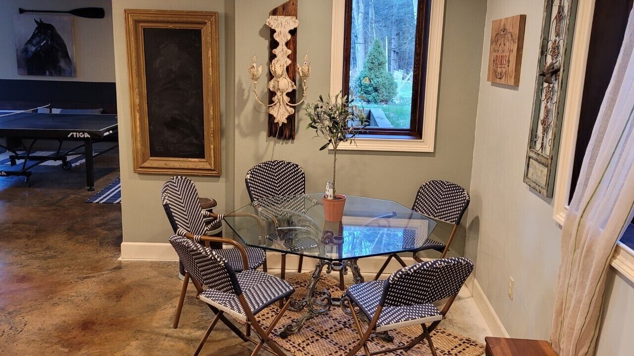 A dining area with a glass table surrounded by patterned chairs, a decorative wall piece, and a view of the outdoors through a window.