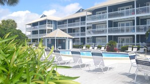 A multi-story hotel with a pool area, including lounge chairs and a small gazebo.
