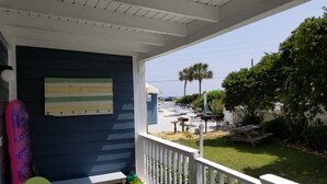 A covered porch with a view of a pool area and a beach.