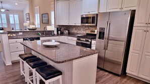A modern kitchen with white cabinets, granite countertops, stainless steel appliances, and a central island with bar stools.