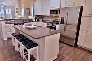 A modern kitchen with white cabinets, granite countertops, stainless steel appliances, and a central island with bar stools.