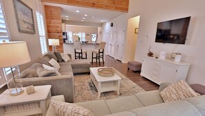A living room with a sofa, a coffee table, a TV, and a kitchen in the background.