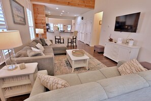 A living room with a sofa, a coffee table, a TV, and a kitchen in the background.