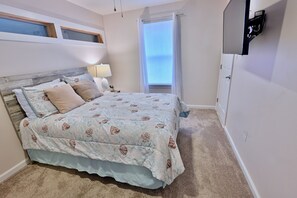 Una camera da letto con un letto, un comodino, una lampada, una finestra con tende e una TV a parete.