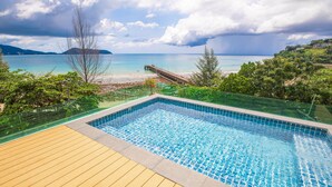 A rectangular swimming pool with a wooden deck in the foreground and a view of the beach and ocean in the background. - Nakalay Seaview Penthouse (Kamala)