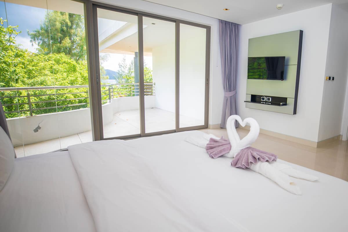 A hotel room with a large bed, a sliding glass door leading to a balcony, and a flat-screen TV mounted on the wall.
