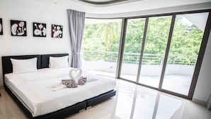 A modern bedroom with a large bed, a balcony with a view of greenery, and artwork on the wall. - Nakalay Seaview Penthouse (Kamala)