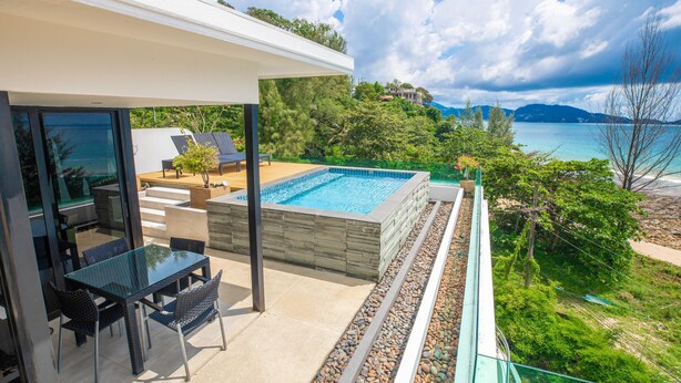 A modern outdoor pool area with a glass table and chairs, surrounded by a stone deck and a view of the sea and hills. - Nakalay Seaview Penthouse (Kamala)