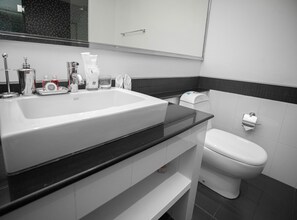 Un baño moderno con un lavamanos grande blanco, una encimera negra, un inodoro blanco y un dispensador de toallas.