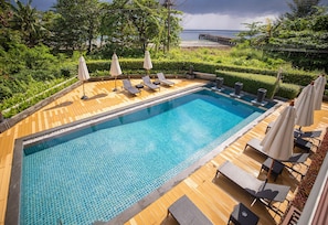 A rectangular swimming pool with a tiled edge, surrounded by wooden decking and lounge chairs with umbrellas.