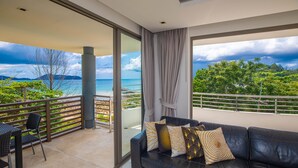 A balcony with a view of the sea and mountains, a black leather sofa with patterned cushions, and a dining area with chairs. - Nakalay Seaview Penthouse (Kamala)