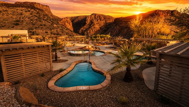 Resort com várias piscinas, um deck de madeira e montanhas ao fundo.
