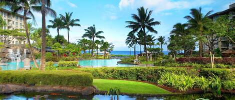 A resort with a swimming pool, palm trees, and a view of the ocean.