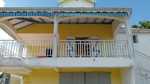 Un immeuble de deux étages doté d’un balcon, d’une grande porte grise et d’un mur jaune.