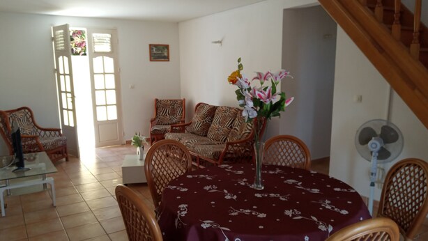 Un coin repas avec une table ronde recouverte d’une nappe à motifs floraux, entourée de chaises en osier. Un vase rempli de fleurs est posé sur la table.