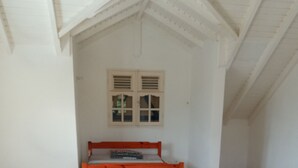 Une chambre avec un lit simple, des murs blancs, une fenêtre avec des volets et un plafond en pente.