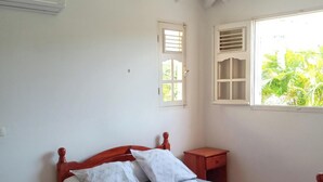 Un lit avec un cadre en bois et une couvre-lit à motifs, une fenêtre avec des stores et un escalier avec des rampes blanches.
