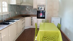 Une cuisine compacte avec des meubles blancs, un four à micro-ondes, un four traditionnel, un évier et une table à manger avec des chaises.