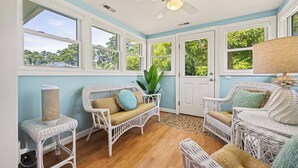 A room with wicker furniture, large windows, and a ceiling fan.