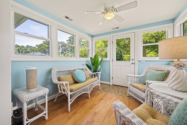 A room with wicker furniture, large windows, and a ceiling fan.