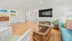 A modern living room with a flat-screen TV, wicker furniture, a blue sofa, and a potted plant.