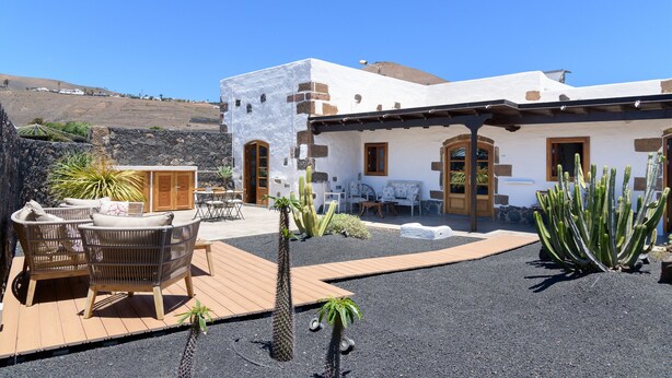 A building with a patio area featuring wicker furniture, a wooden deck, and cacti. - Luciana, La Casa del Medianero (Macher)