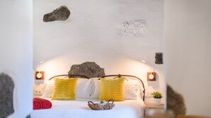 Un dormitori amb un llit, almoines, una tauleta de nit amb una planta i una paret amb roques.