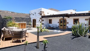 Un edificio con un patio amoblado con muebles de mimbre, una terraza de madera y cactus.