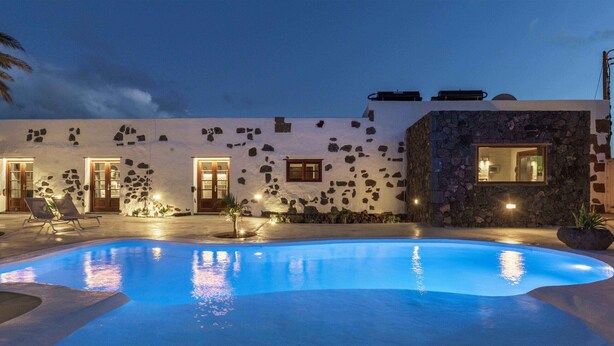 Zona de piscina con pared de piedra, piscina y una silla de descanso.