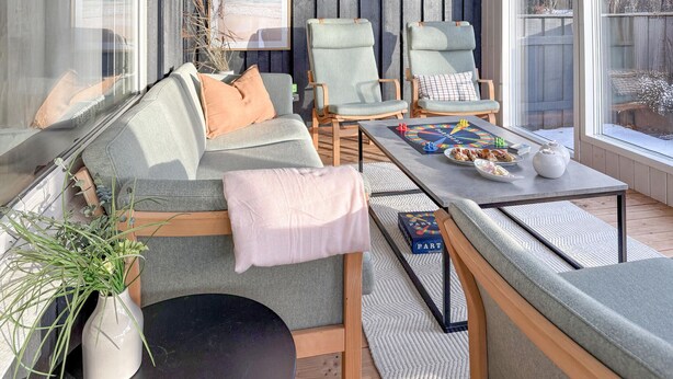 Un espace de détente extérieur accueillant, avec un canapé, deux fauteuils, une table avec des jeux de société et une plante en pot.