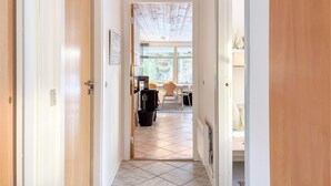 Un couloir mène à une salle à manger donnant sur l’extérieur, avec une table et des chaises, et un radiateur fixé au mur.
