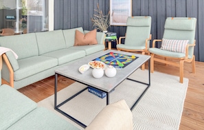 A modern living room with a grey sofa, two armchairs, a coffee table with board games, and a decorative vase.