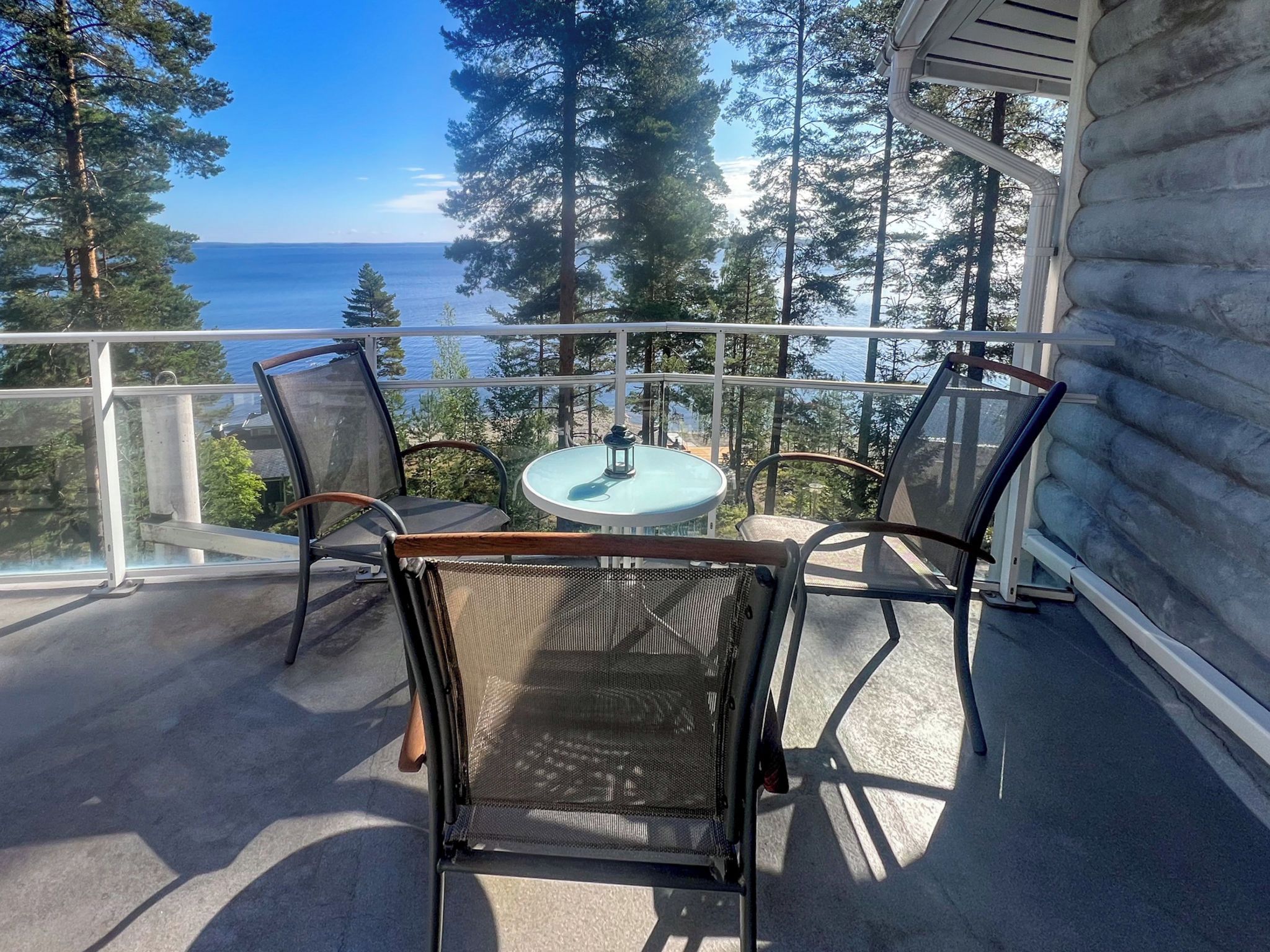 A balcony with a round table and two chairs, overlooking a body of water and forested area.