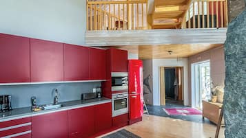 A modern kitchen with red cabinets, a red refrigerator, and a wooden staircase leading to an upper level.