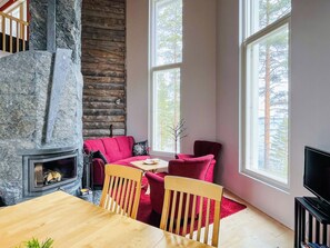 Una habitación acogedora con chimenea de piedra, un sofá rojo, una mesa de comedor de madera y ventanas grandes.