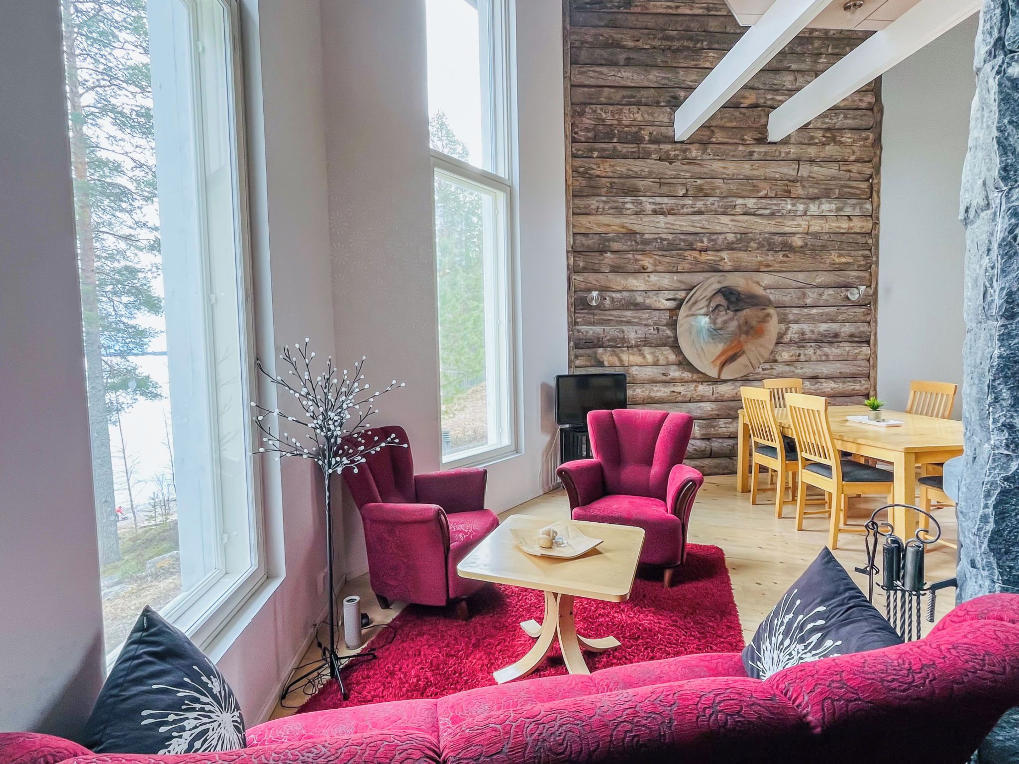 A modern living room with a red sofa, two red armchairs, a wooden dining table, and a stone wall with a circular artwork.