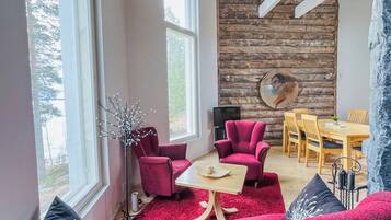 A modern living room with a red sofa, two red armchairs, a wooden dining table, and a stone wall with a circular artwork.