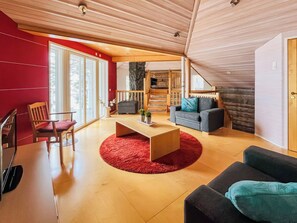 A modern living room with a wooden ceiling, a red accent wall, and a large window.
